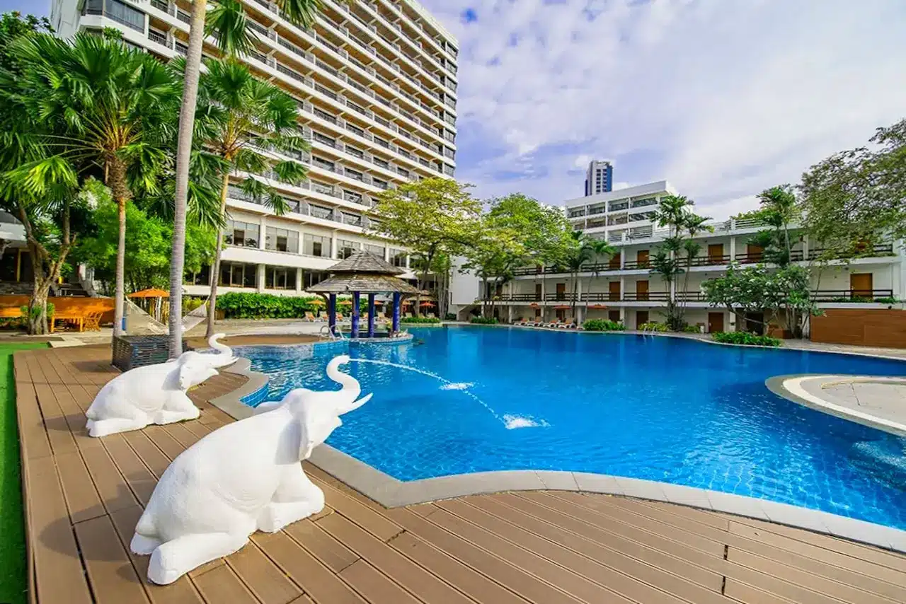Großer Pool mit Liegen und Sonnenschirmen vor dem Cosy Beach Hotel in Pattaya South – imposantes Gebäude im Hintergrund.