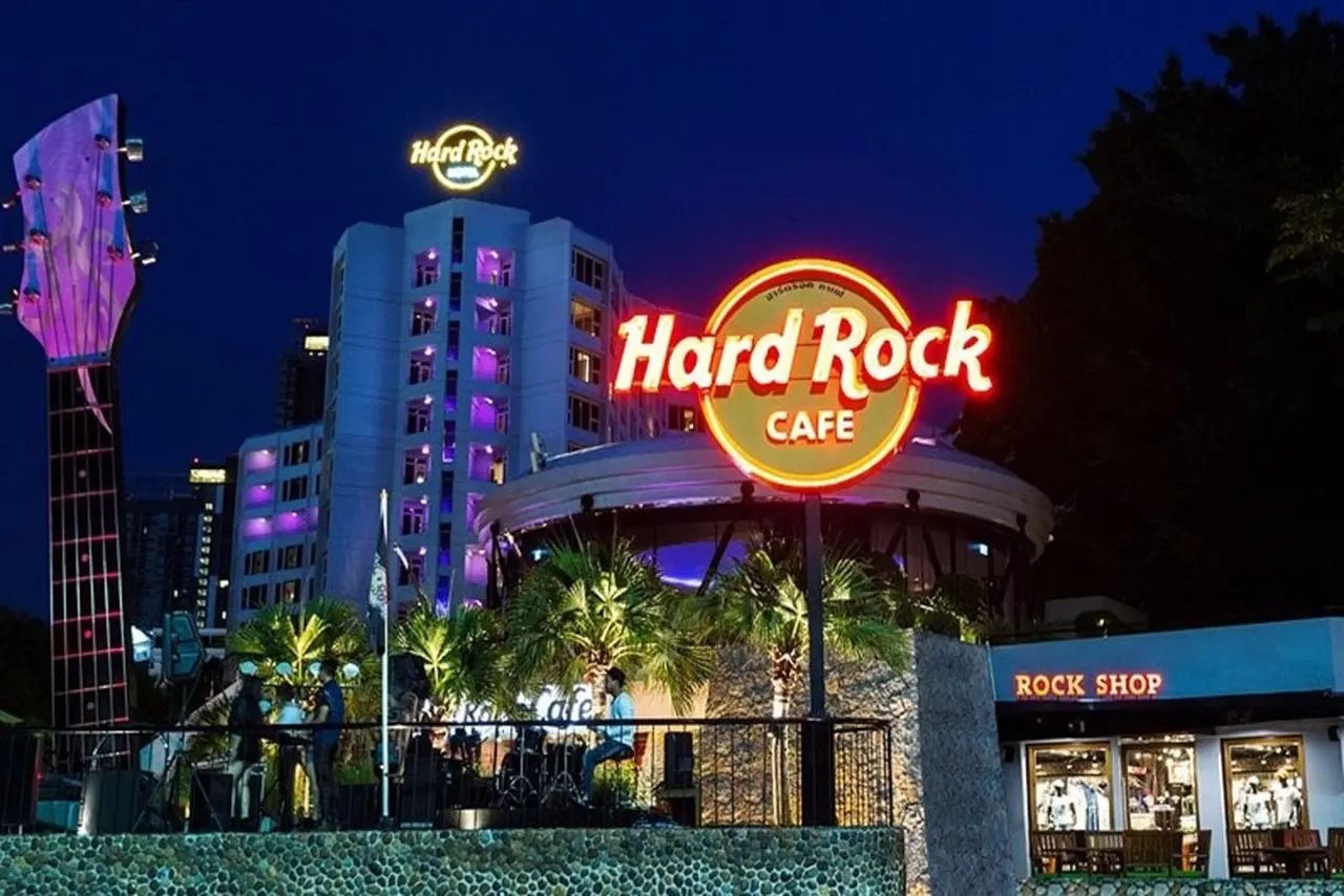 Beleuchtete Front des Hard Rock Cafe Pattaya bei Nacht mit großer Gitarre und Werbeschildern, im Hintergrund das Hard Rock Hotel.