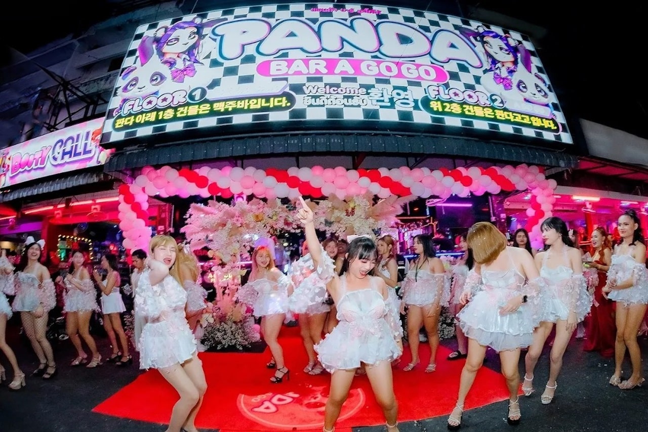 The exterior view of the Panda Bar a go-go at night with illuminated shield and dancing hostesses in front of the entrance to red carpet.