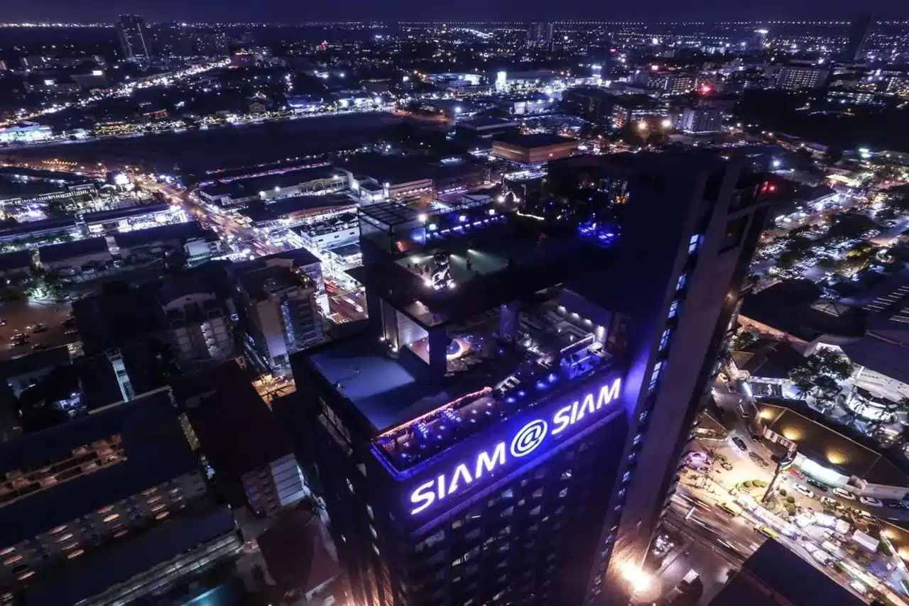 Nachtansicht des Siam Siam Design Hotel Pattaya mit Infinity-Pool, beleuchtetem Hoteldach und Barbereich.